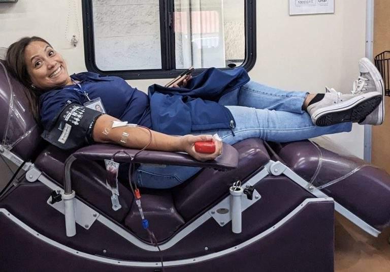 Donor lays in the chair and smiles for the camera as tubing connects her arm to the bag of blood.