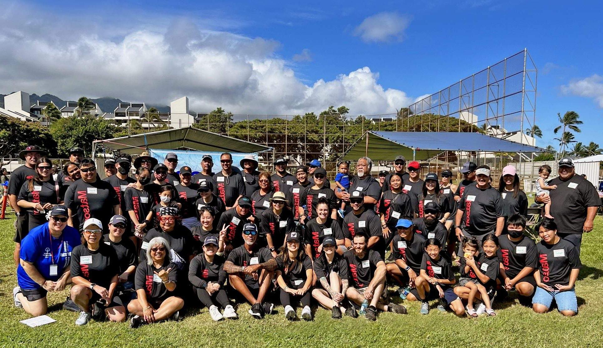 澳博体育app的志愿者们穿着印有红色澳博体育app标志的黑色t恤，以垒球场的挡板为背景，摆姿势合影.