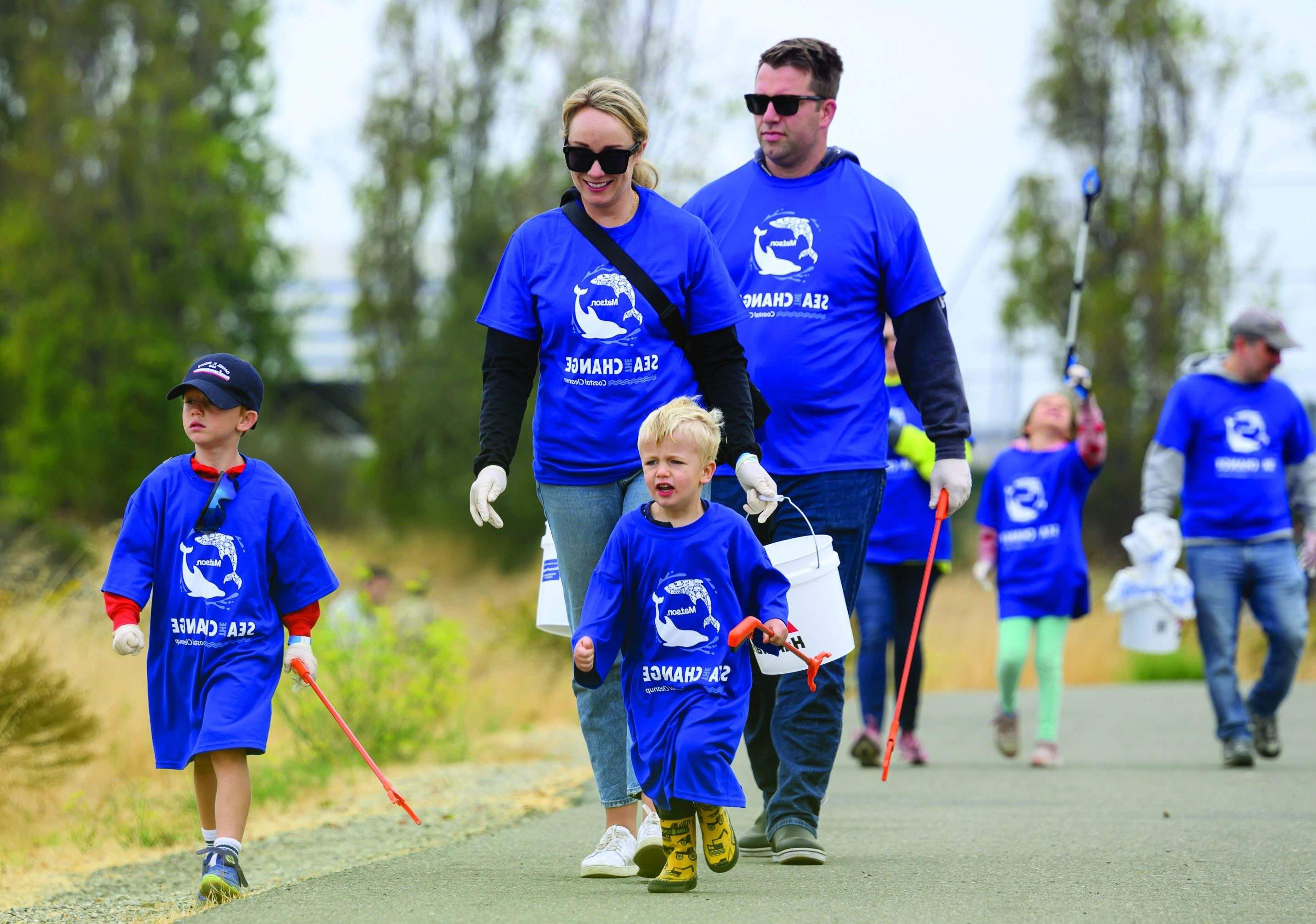 有两个小男孩的家庭穿着超大号的衣服, 蓝色澳博体育app下载“Sea The Change”t恤带着抓手和水桶走到清理现场.