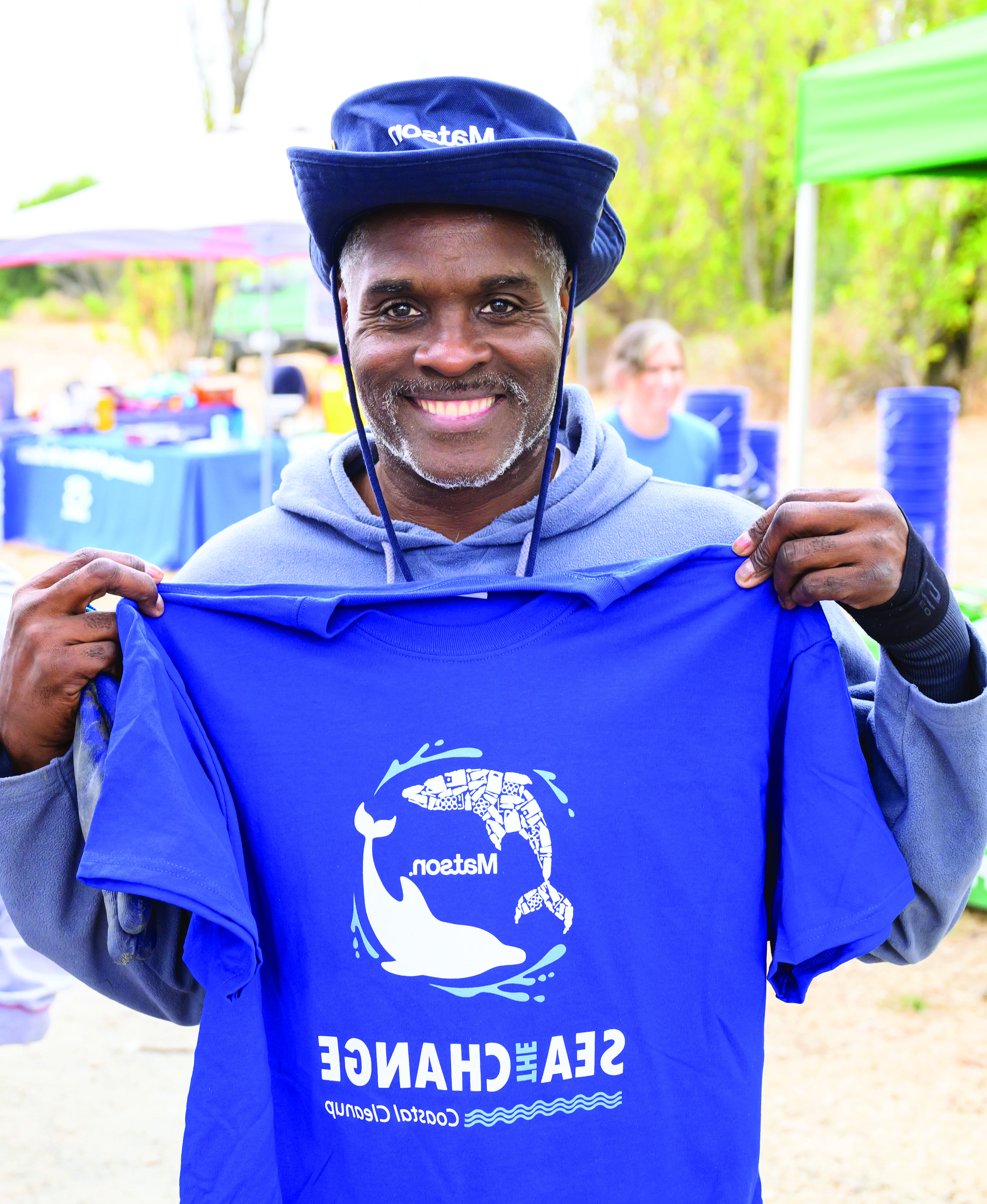 志愿者戴着印有蓝色澳博体育app标志的手，拿着一件印有两只海豚环绕澳博体育app标志和“Sea the Change”字样的蓝色t恤."