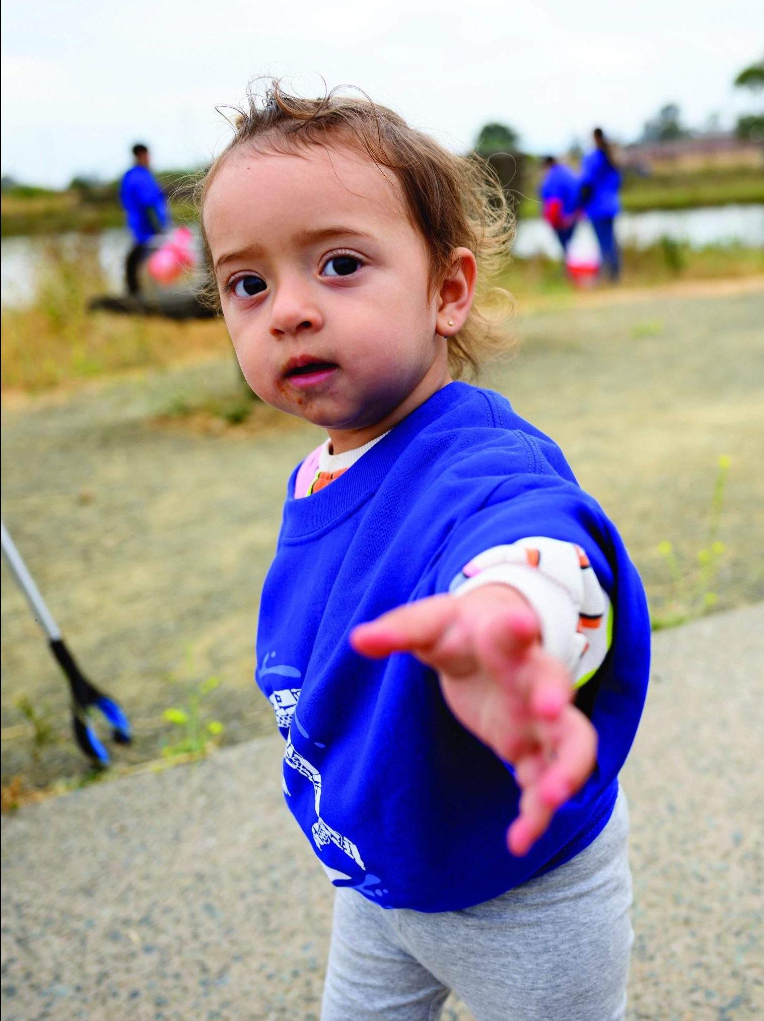 一个穿着蓝色澳博体育app下载“Sea The Change”t恤的小孩在奥克兰河口伸出援助之手.