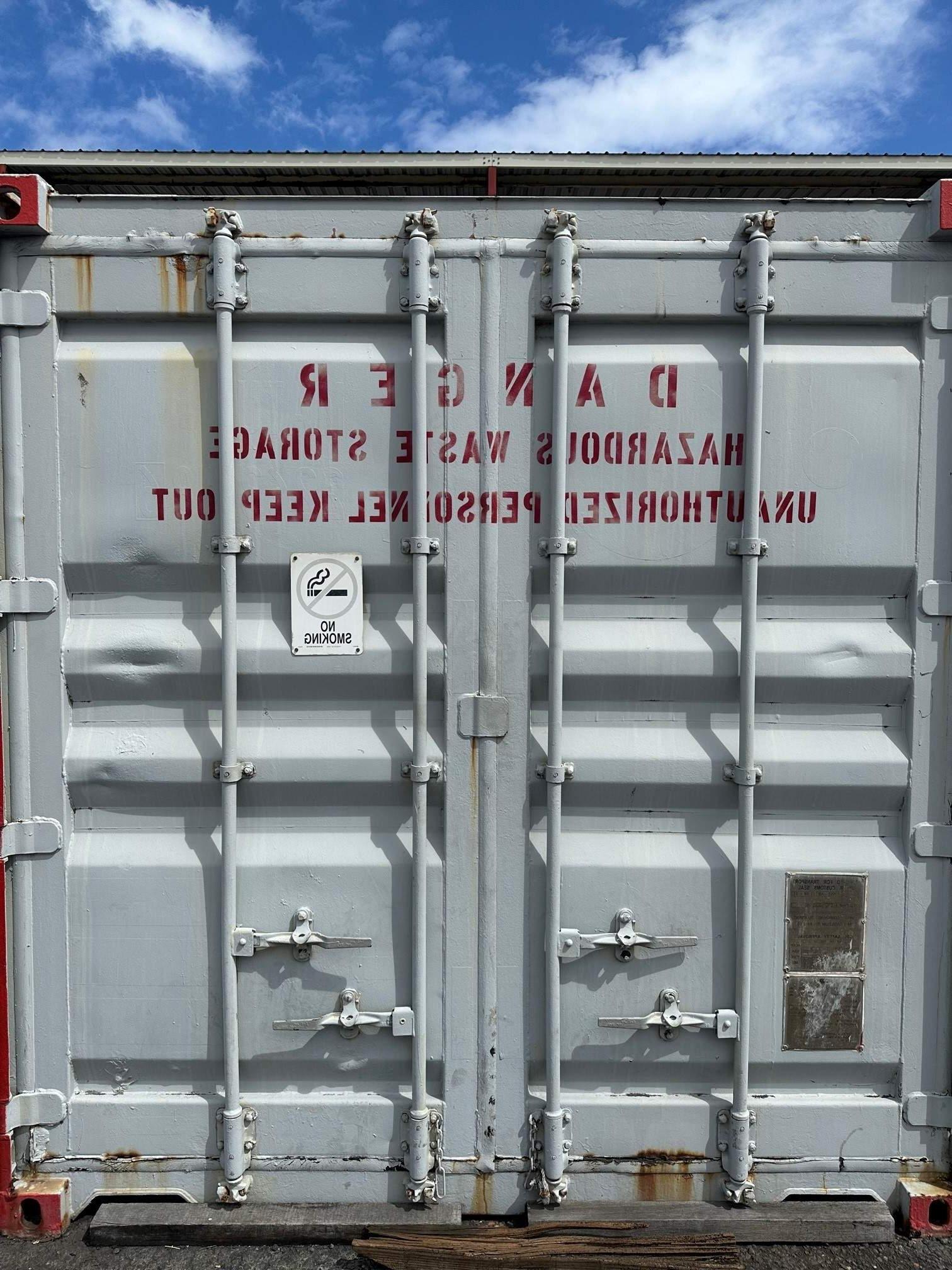 Gray container marked "DANGER Hazardous Waste Storage Unauthorized Personnel Keep Out" in red sits at a terminal.