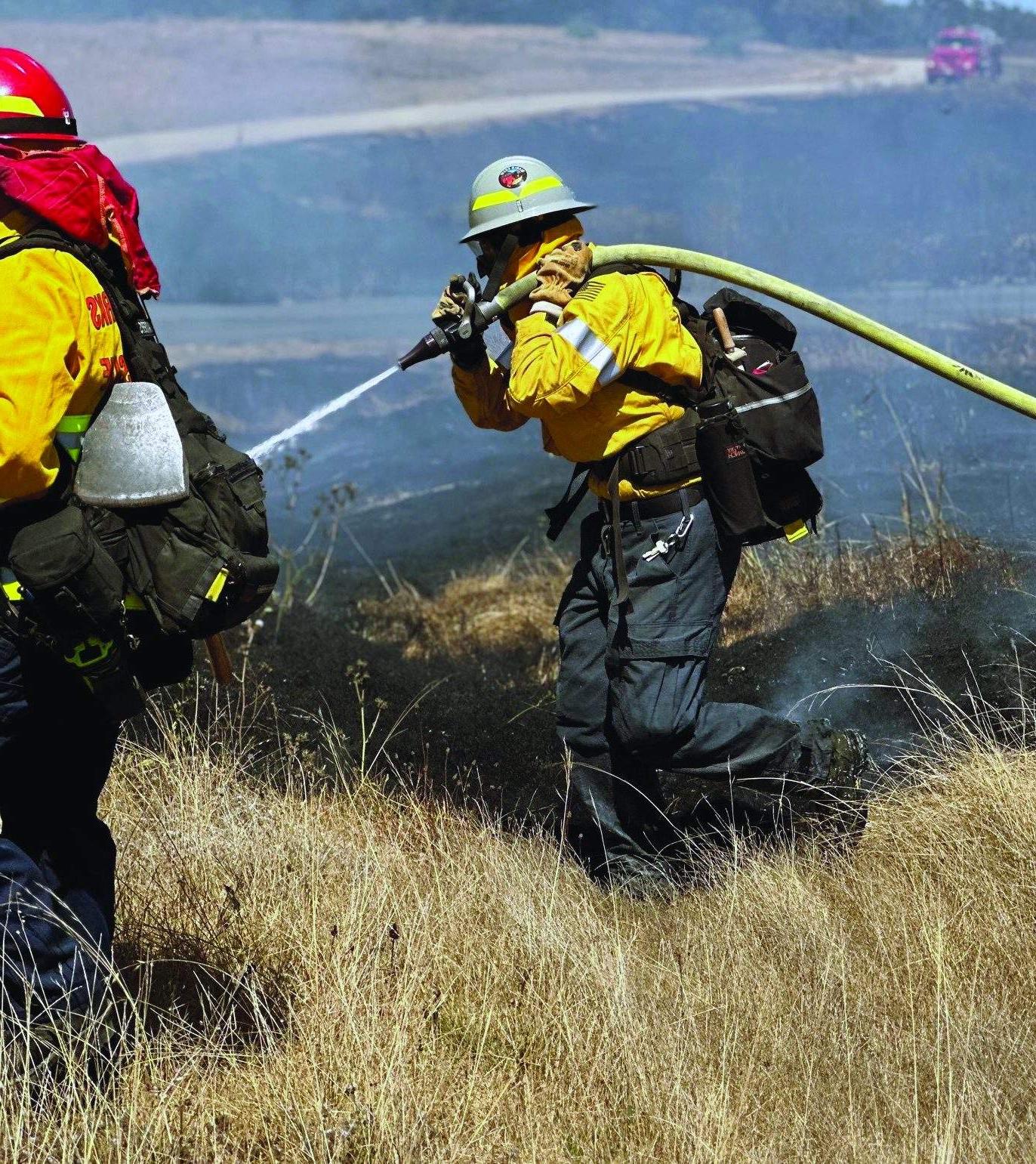 埃里卡·布拉德利肩上扛着一根水管，帮助扑灭一场草火.